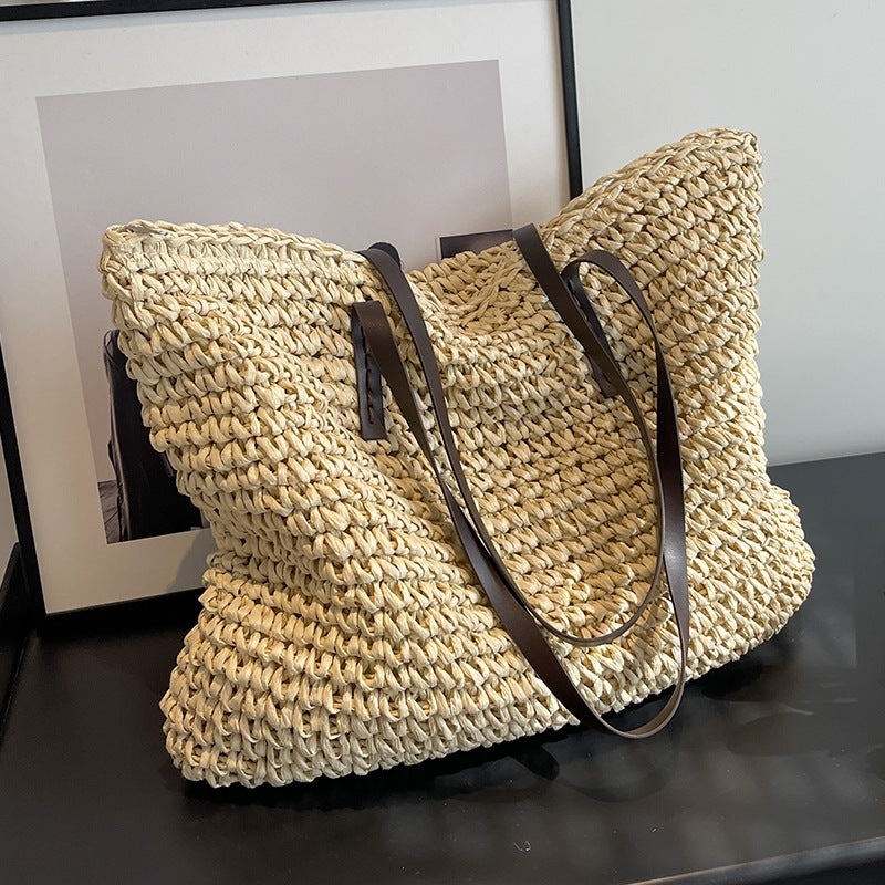 Woven shoulder beach bag in light beige with dark handles and curved shoulder strap