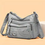 Gray PU leather crossbody bag with multiple zippers, braided front pocket, and ring accents