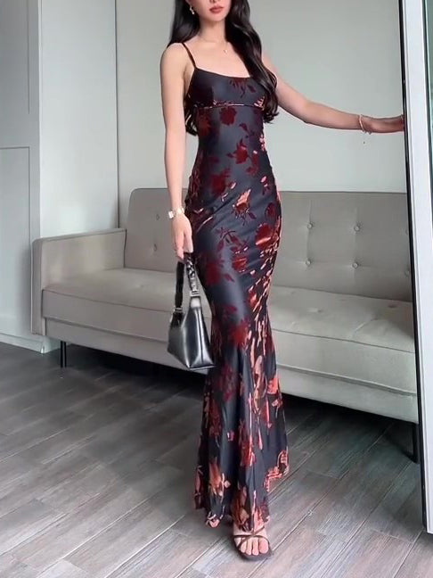 Black floral fitted maxi dress with thin straps and side slit hem, holding handbag