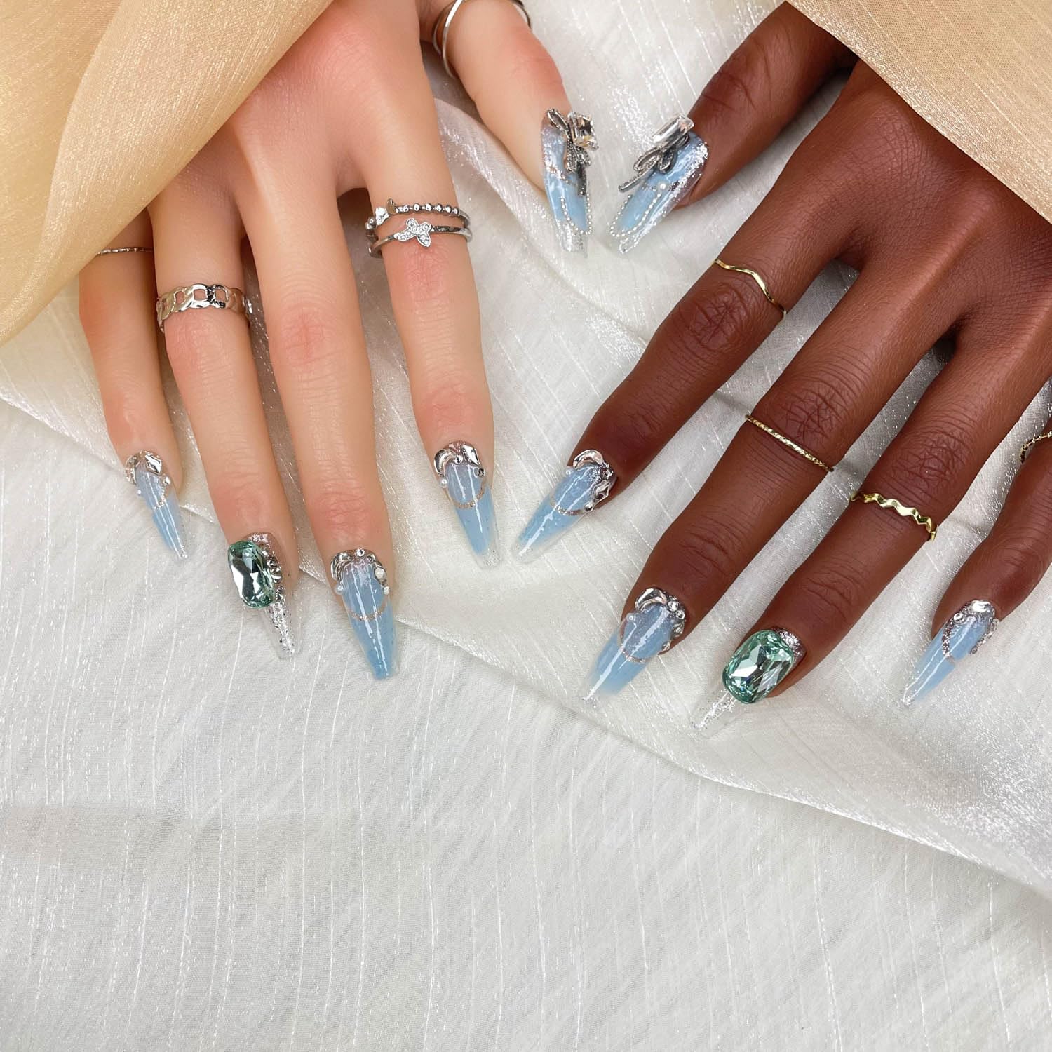 Press-on nails set with light blue gradient, silver tips, and green crystal accents