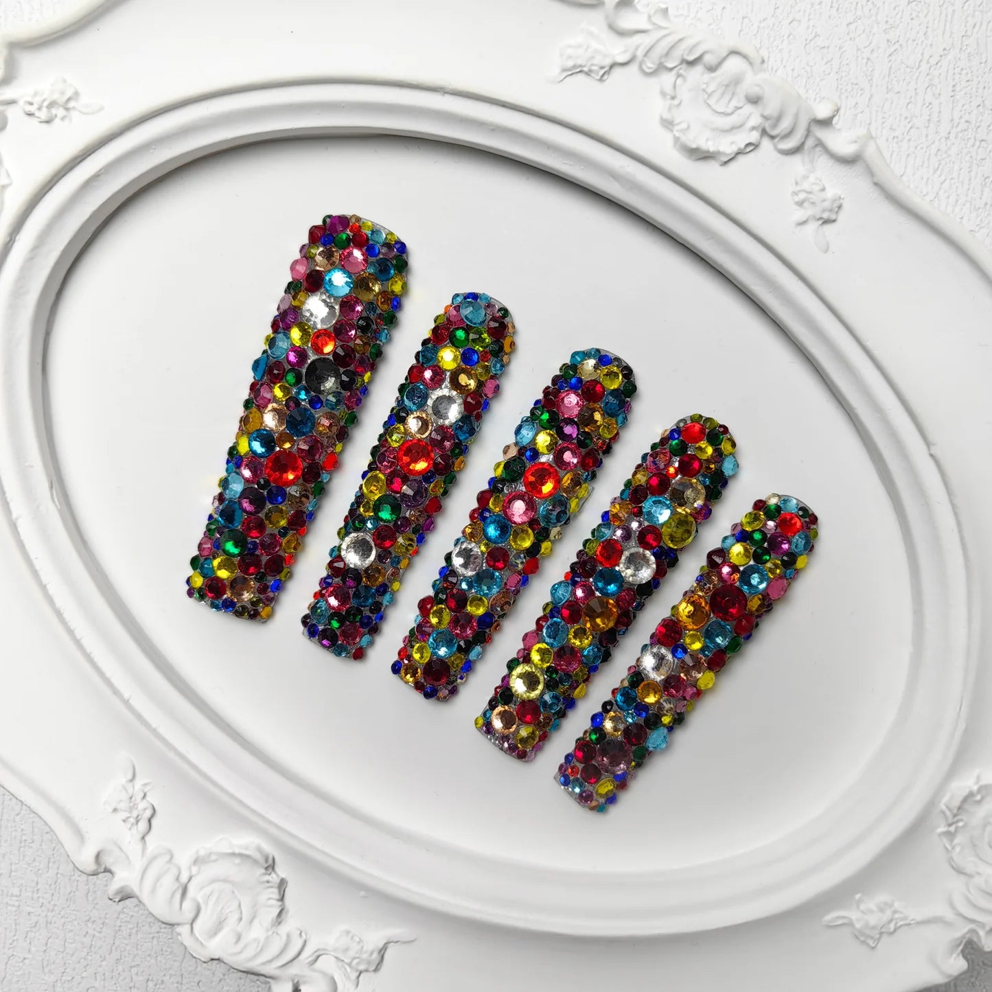 Long rhinestone press-on nails arranged on a plate, multicolor mosaic bead pattern